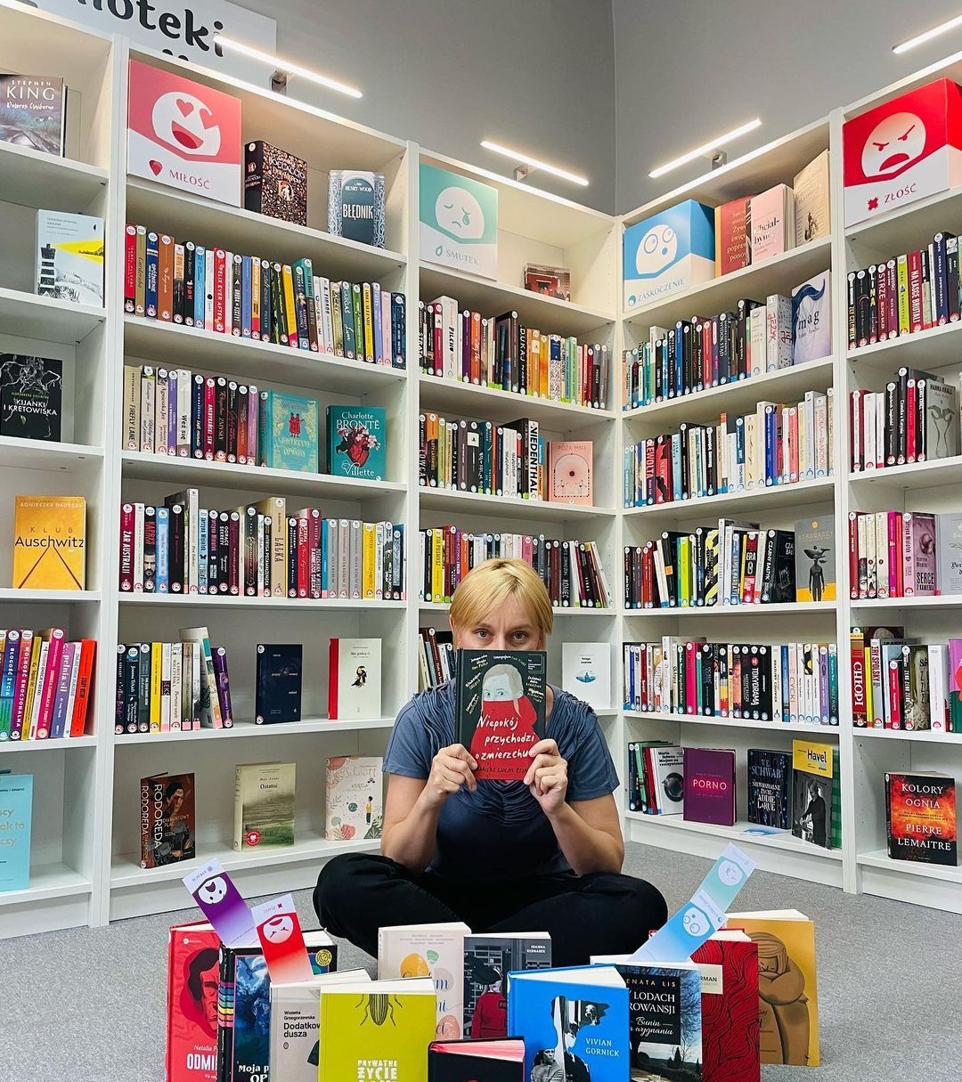 Un lecteur assis au milieu des rayonnages, un livre ouvert devant lui